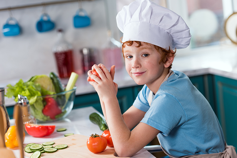 cute little boy in chef hat smiling at camera while cooking in k