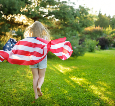 American flag waving outdoors with a little girl against a blue sky