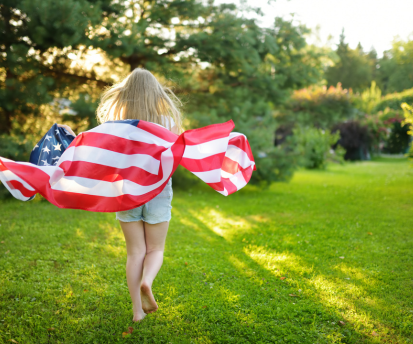 American flag waving outdoors with a little girl against a blue sky